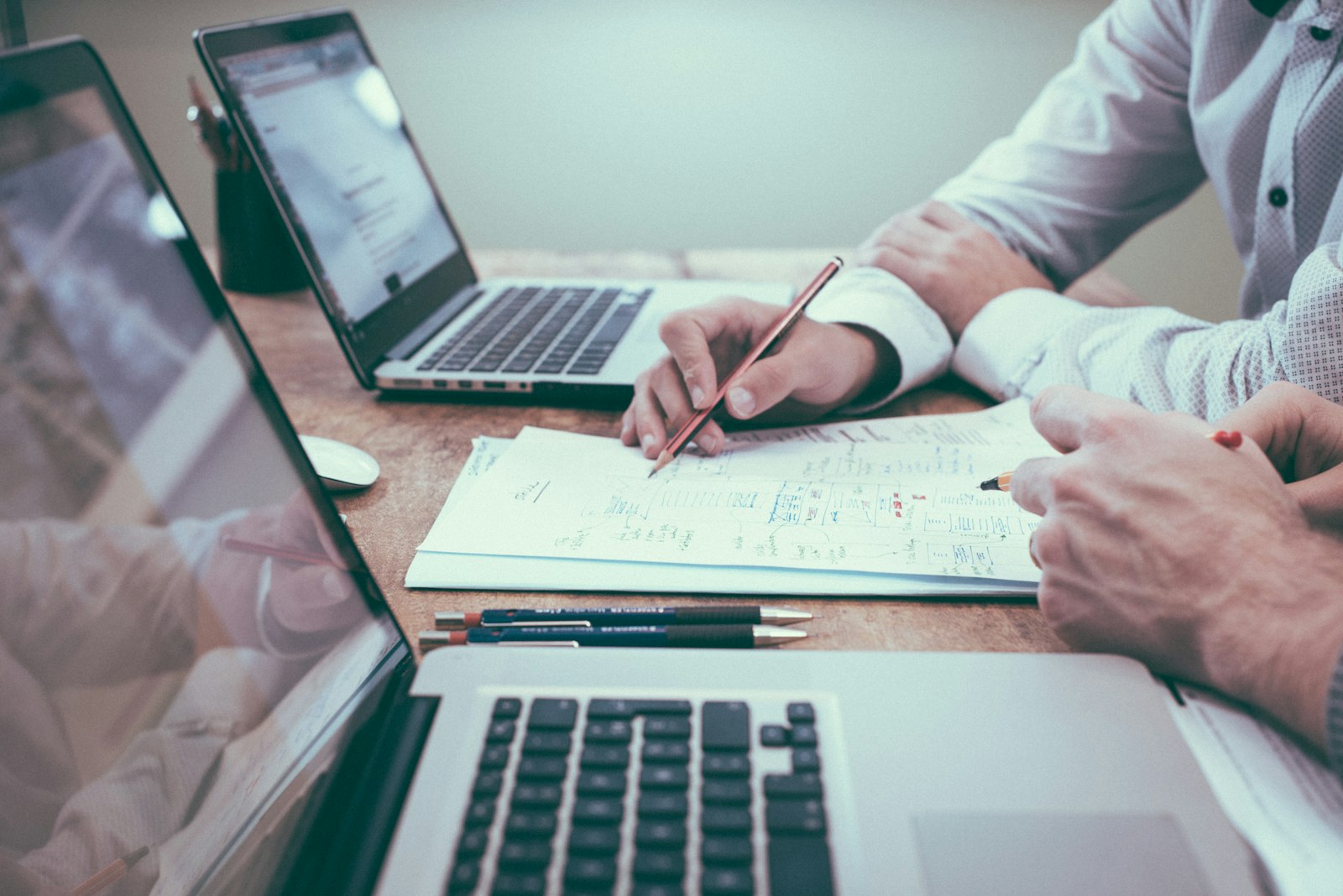 Two people reviewing paperwork beside laptops on a desk